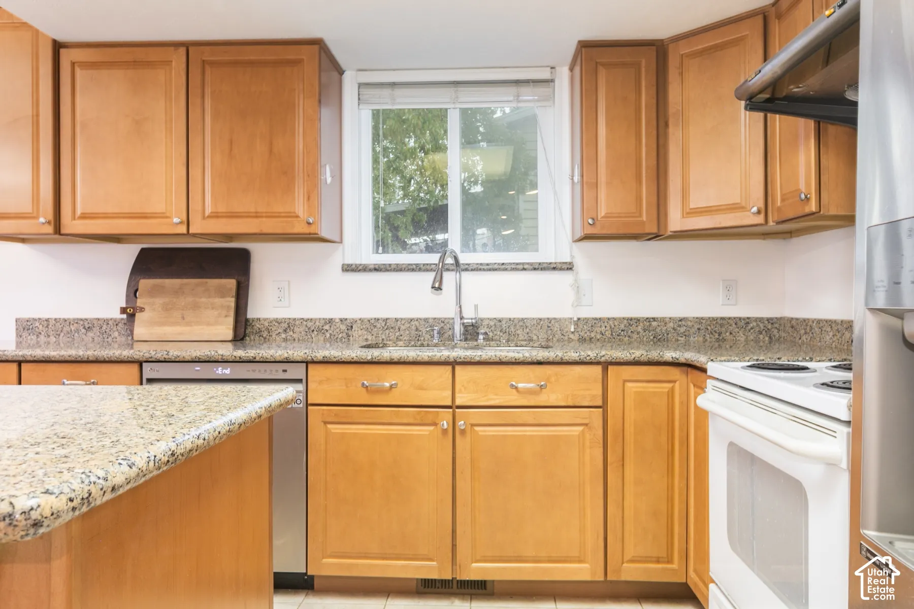 Kitchen featuring wood cabinetry, stone-surface countertops, a stainless steel dishwasher, a white range, and a single-basin undermount sink with a pull-down faucet
