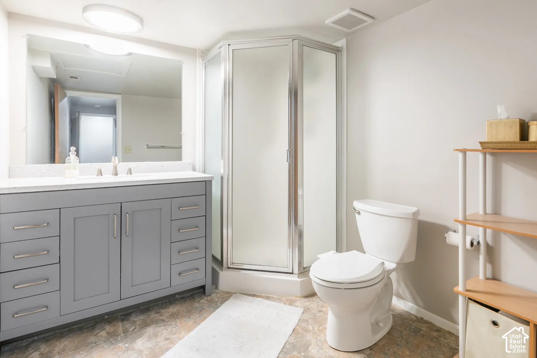 Grey vanity featuring a light-toned countertop, corner shower enclosure with frosted glass doors, and a large-format vanity mirror