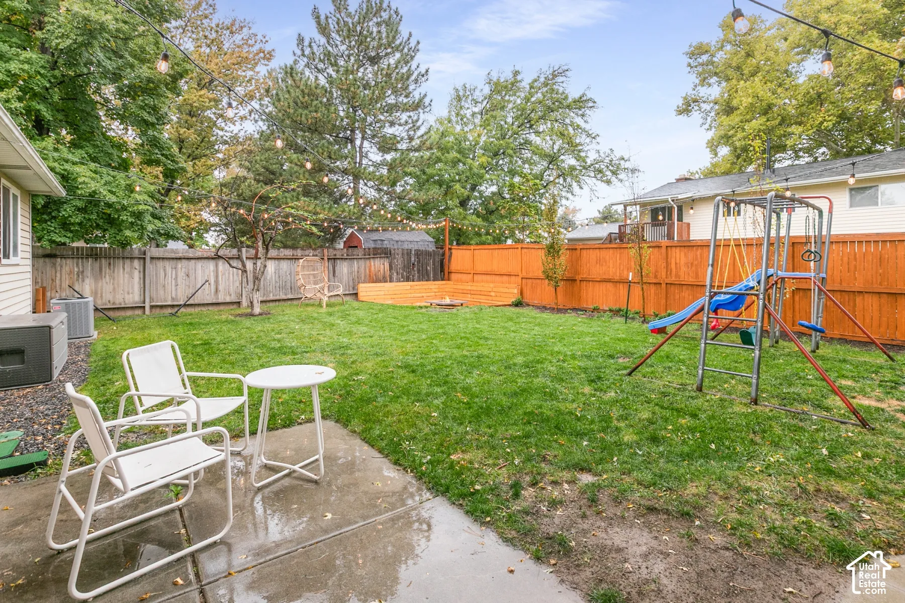 Fenced backyard featuring a concrete patio, wood-finish privacy fencing, and string lighting