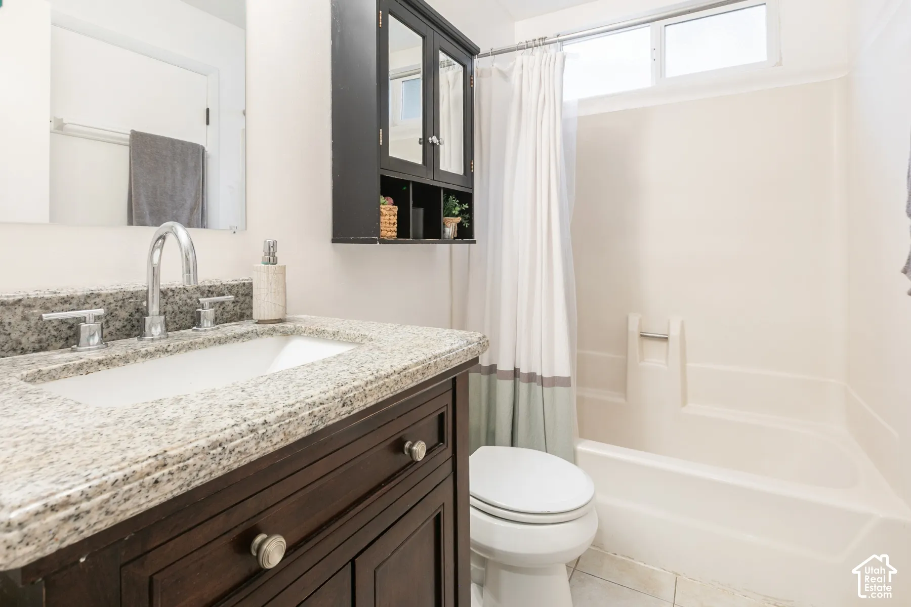 Bathroom featuring a dark wood vanity, speckled stone-finish countertop with an integrated basin, wall-mounted storage cabinet, and a tiled shower-tub combination with a clerestory window