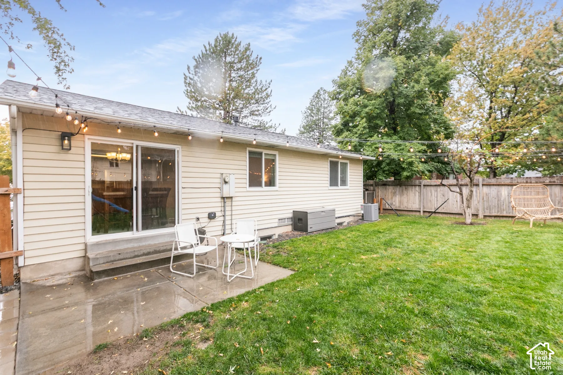 Backyard featuring a concrete patio, exterior siding, sliding glass door, string lighting, and wood privacy fencing