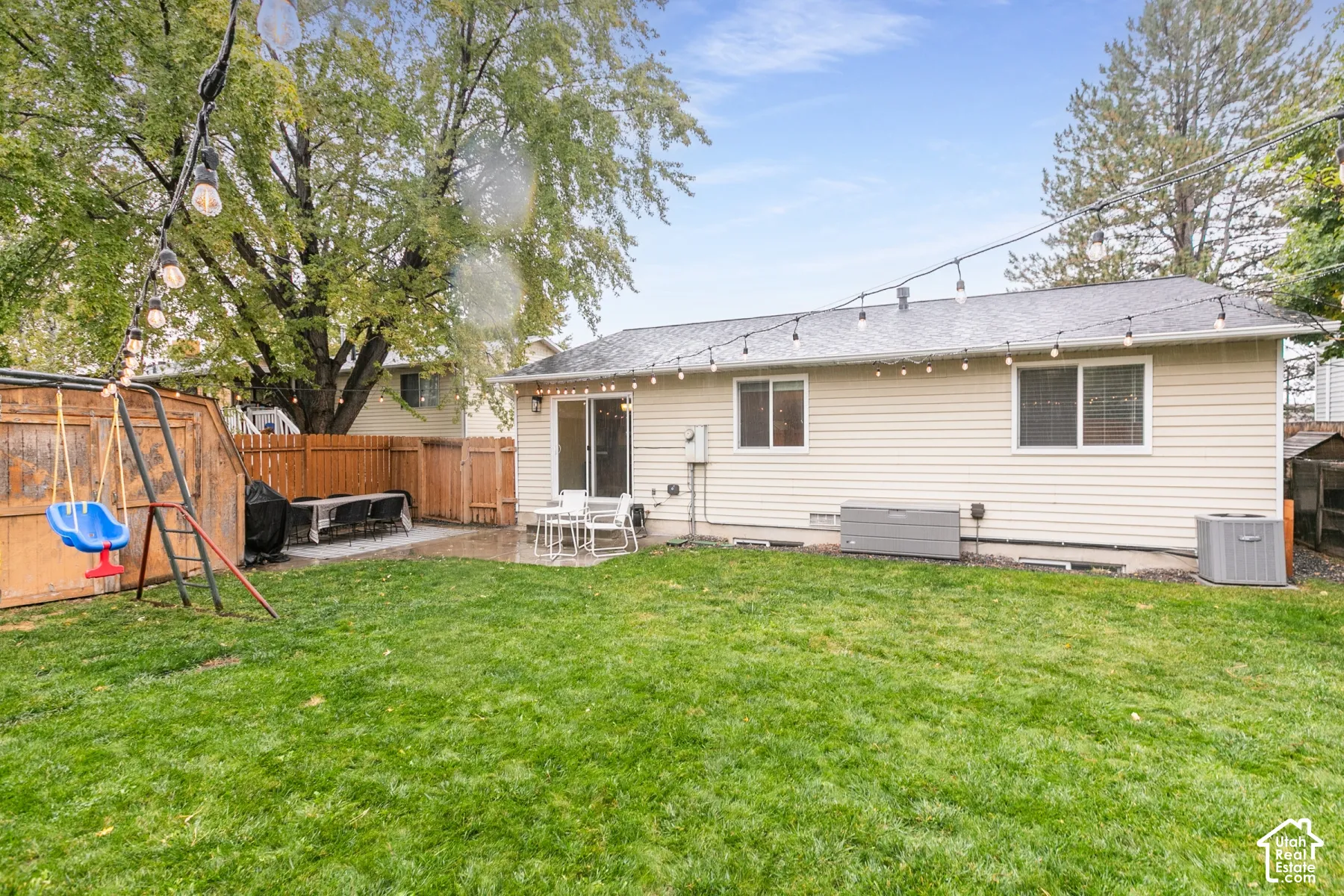 Fenced backyard featuring a manicured lawn, concrete patio, and mature trees