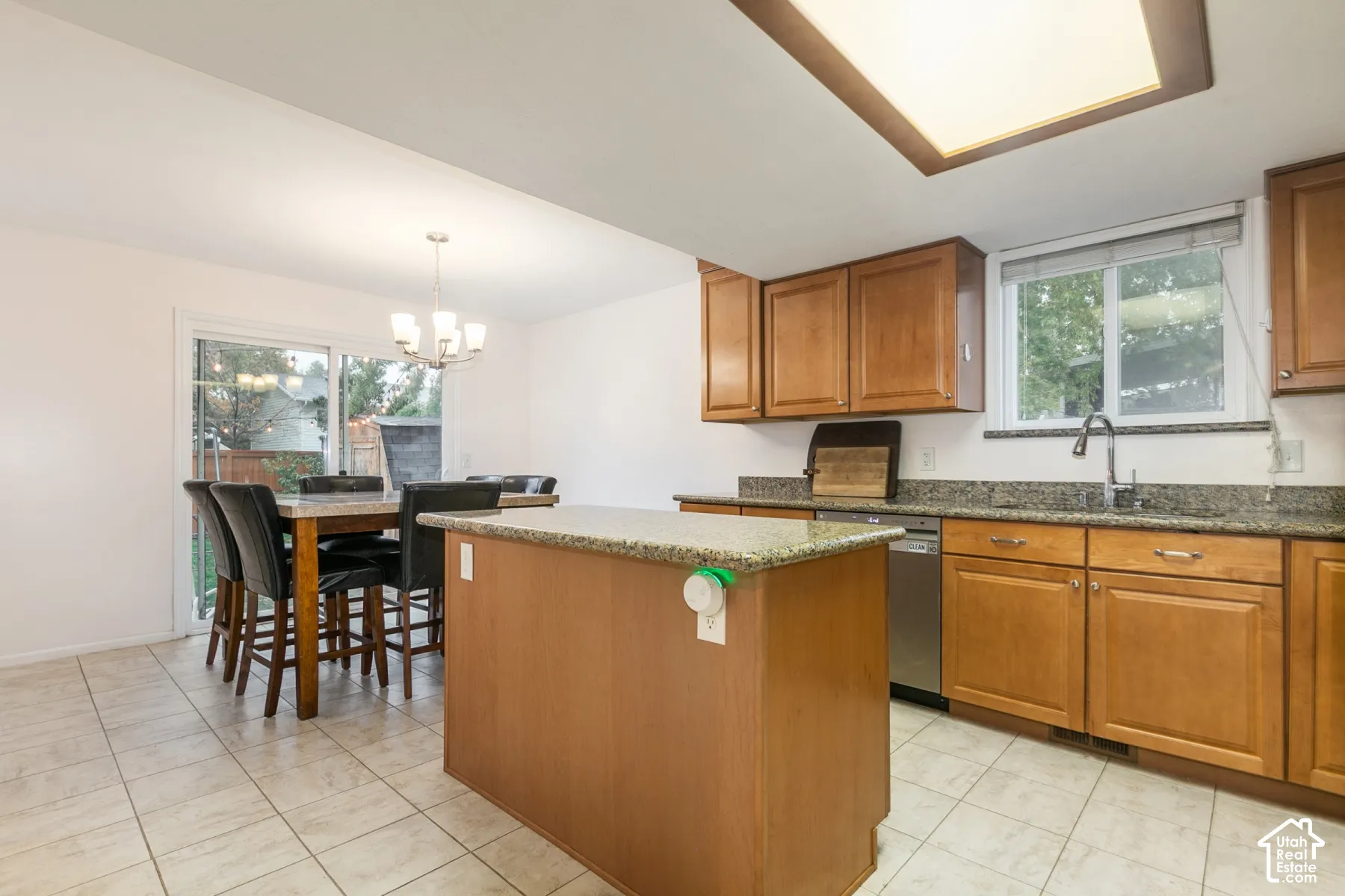 Kitchen featuring a center island, stone-finish countertops, wood-finish cabinetry, stainless steel dishwasher, and tile flooring