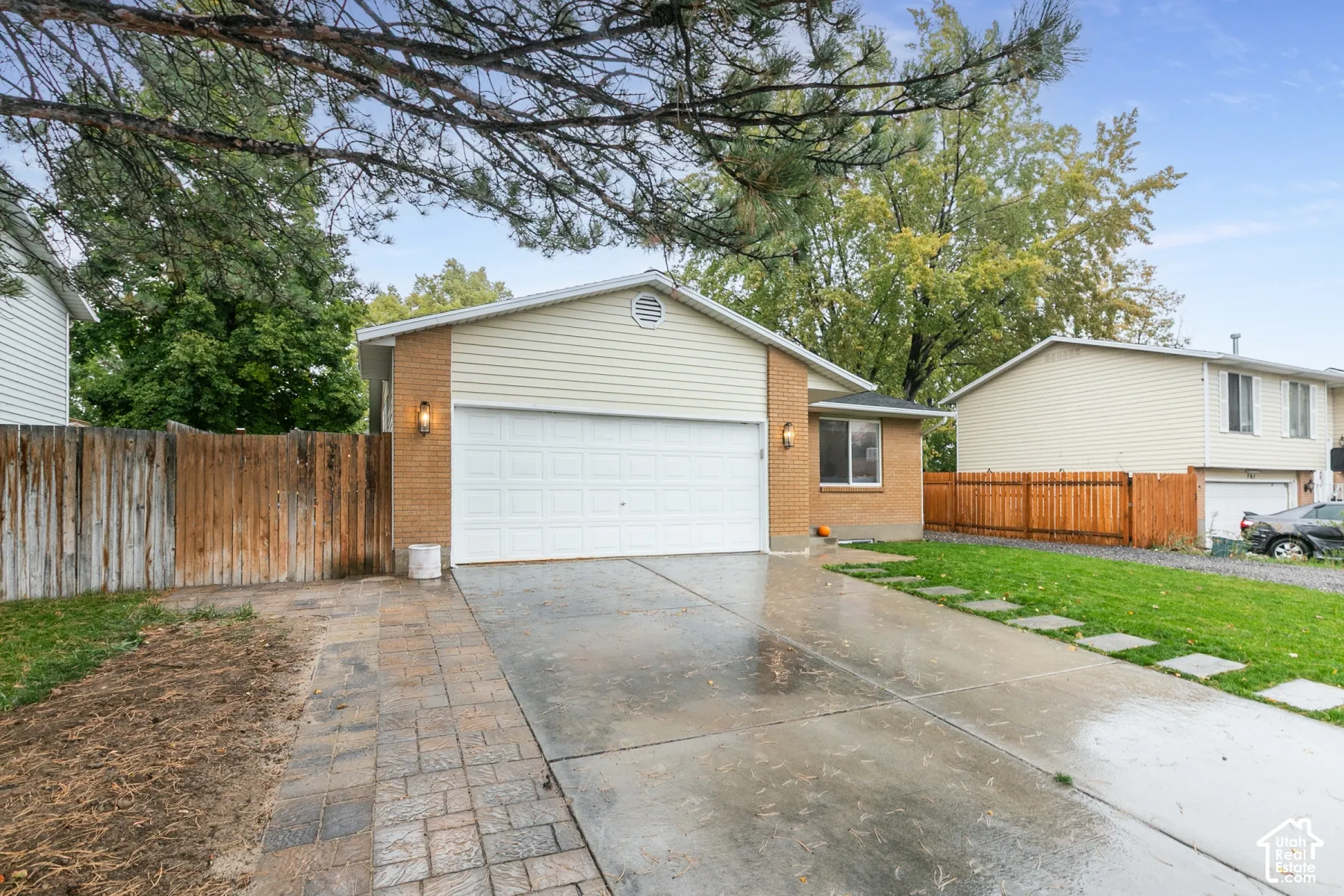Exterior facade featuring brick and horizontal siding, an attached two-car garage, paved driveway, and stone-paver hardscaping
