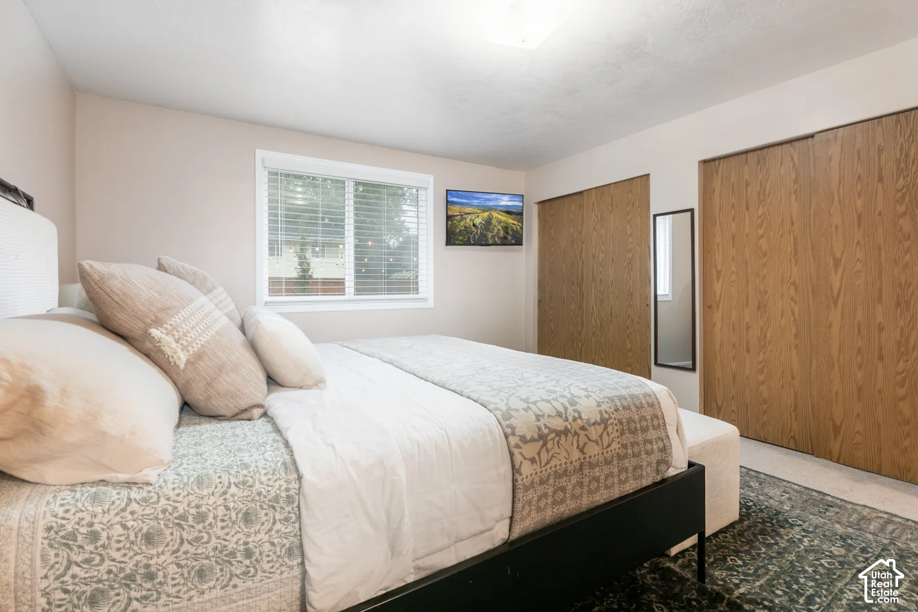 Bedroom featuring dual wood-finish sliding closet doors, neutral-toned walls, and a window equipped with horizontal blinds