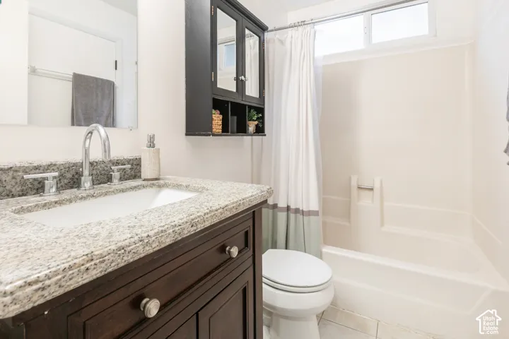Bathroom featuring a dark wood vanity, speckled stone-finish countertop with an integrated basin, wall-mounted storage cabinet, and a tiled shower-tub combination with a clerestory window