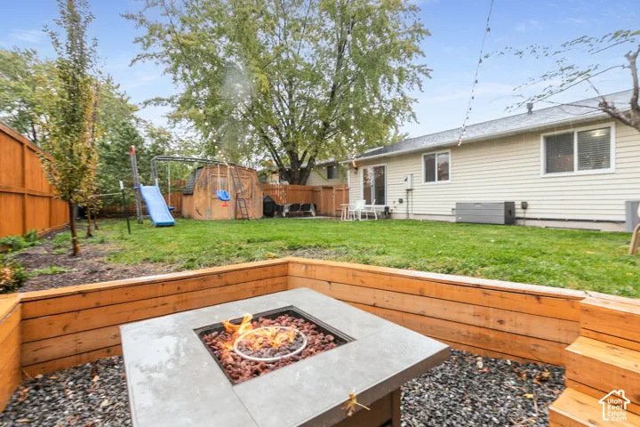 Rear exterior featuring a tiered timber retaining wall, built-in fire pit, manicured lawn, and full wood perimeter fencing