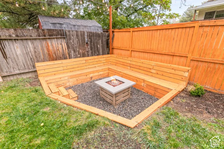 Sunken patio featuring built-in wood-plank bench seating, a square concrete fire pit, and stone ground cover, enclosed by wood privacy fencing