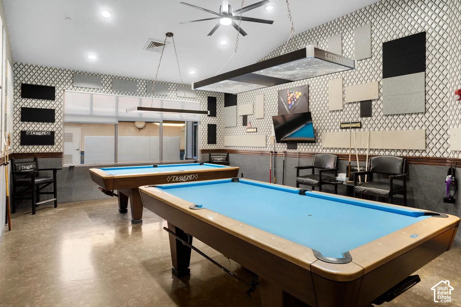 Recreational space featuring geometric-patterned wall coverings, integrated sound-dampening wall panels, polished concrete flooring, suspended task lighting, and recessed ceiling illumination