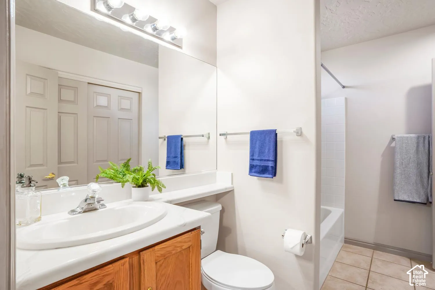 Bathroom featuring a wood-finish vanity with a stone-surface countertop, integrated basin, large wall-mounted mirror, and tile flooring
