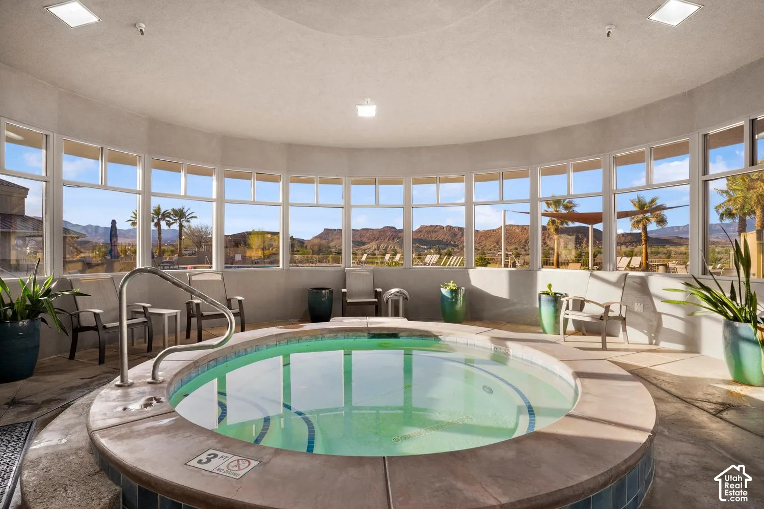 Indoor jetted pool featuring a concrete surround, metal safety railing, expansive wrap-around windows, and mountain scenery