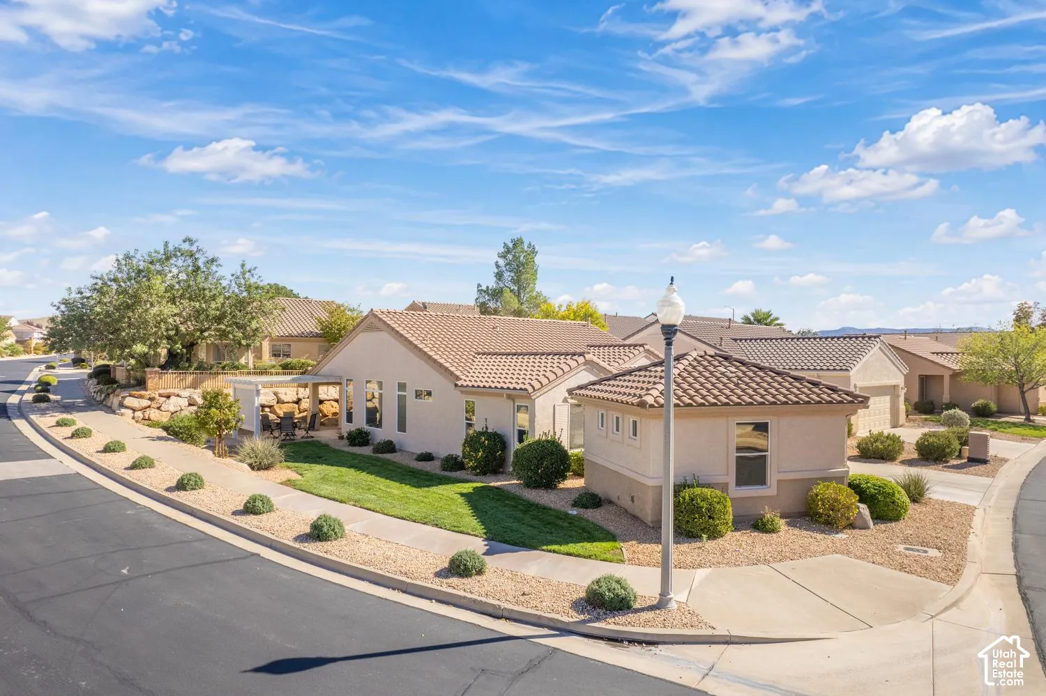 Exterior featuring a tile roof, stucco siding, and a covered patio area with a landscaped lawn and xeriscaped rock borders