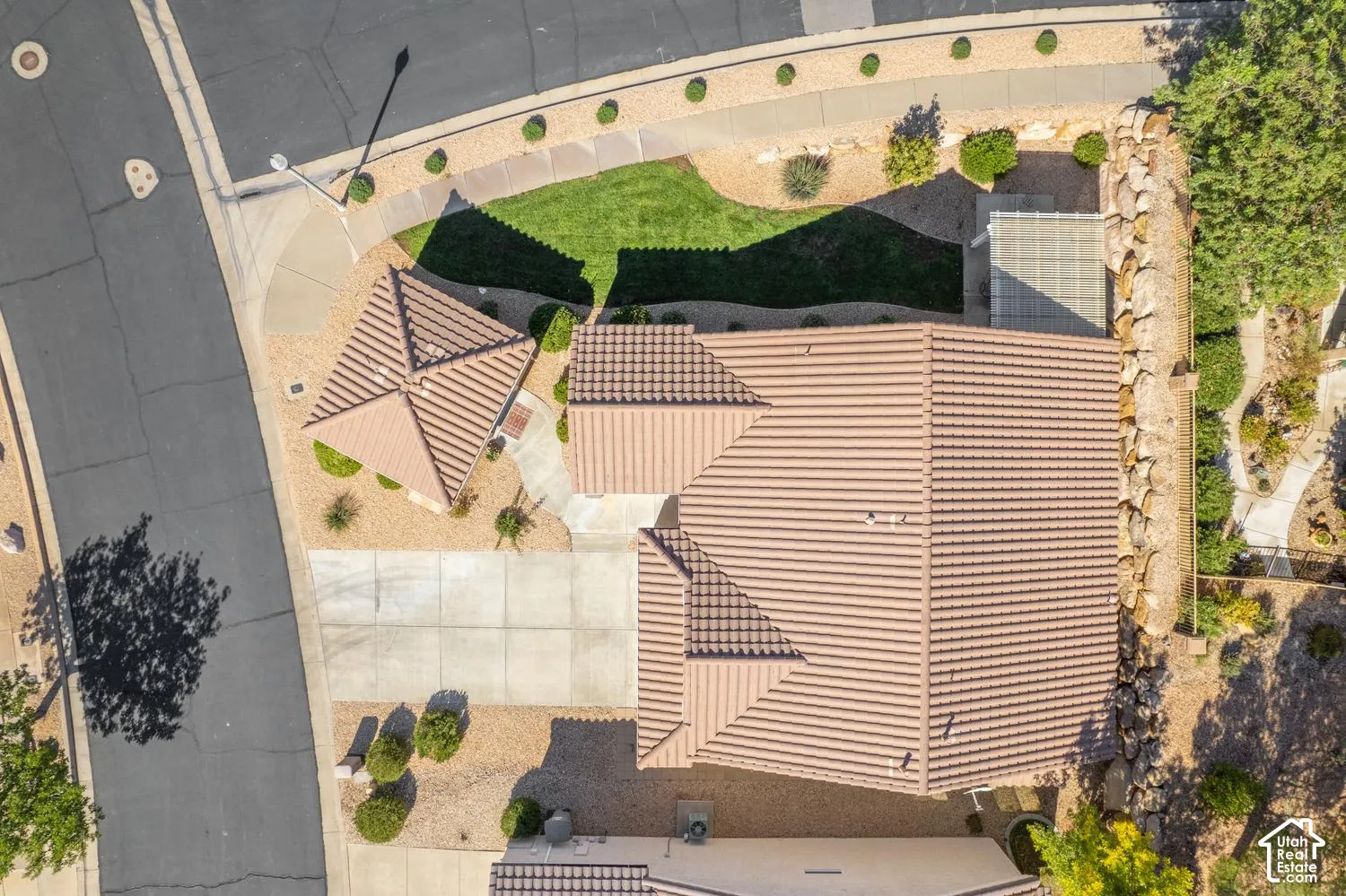 Aerial view of a corner lot property featuring a tile roof, concrete driveway, xeriscaped front yard, and a stone retaining wall