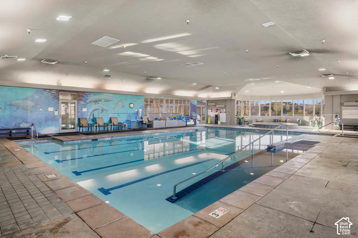 Indoor swimming pool featuring multiple lap lanes, integrated hot tub, extensive tile surround, and large-scale wall mural