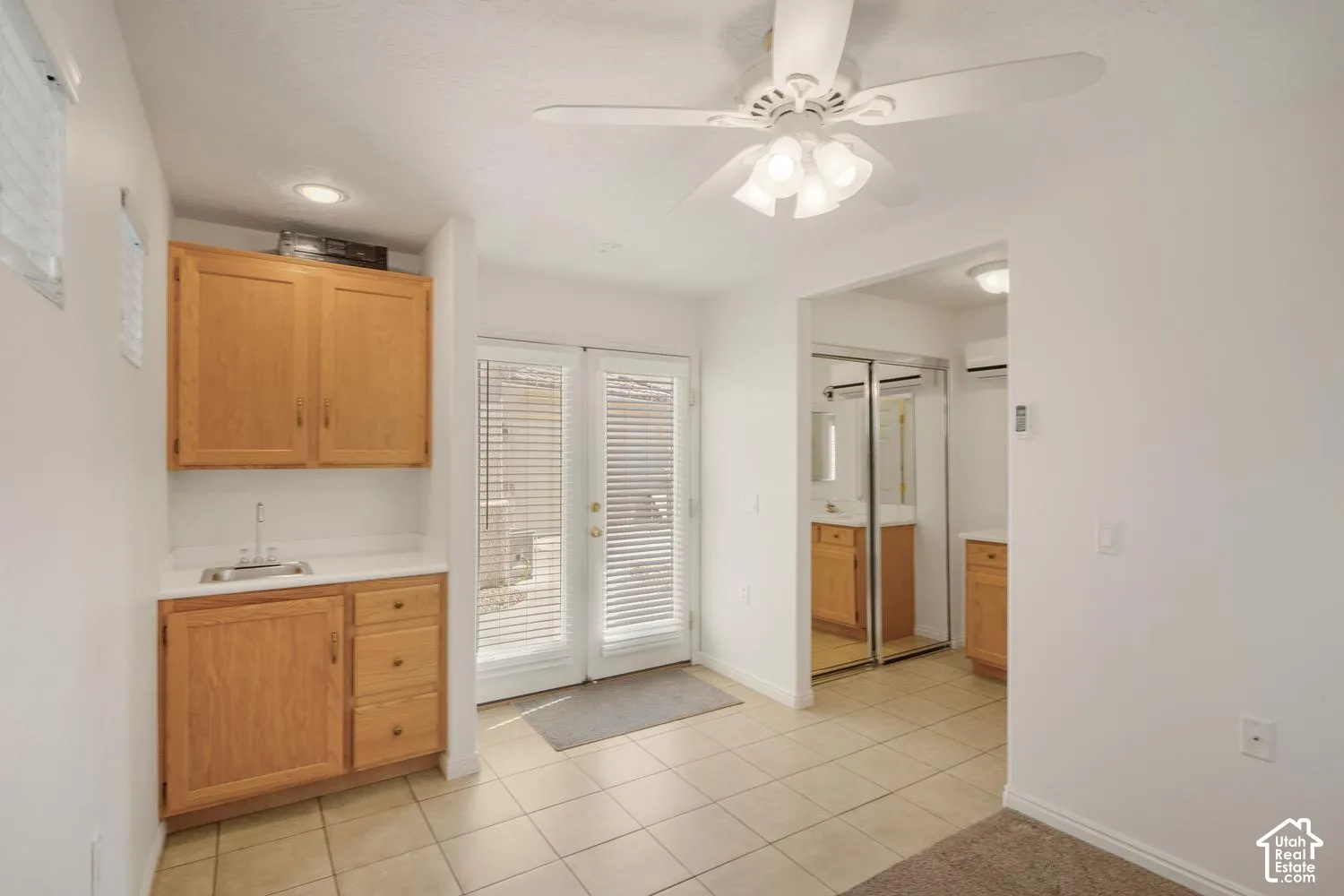 Built-in cabinetry with wood-finish doors, integrated sink, tile flooring, ceiling fan with light fixture, and double glass-paneled exterior doors