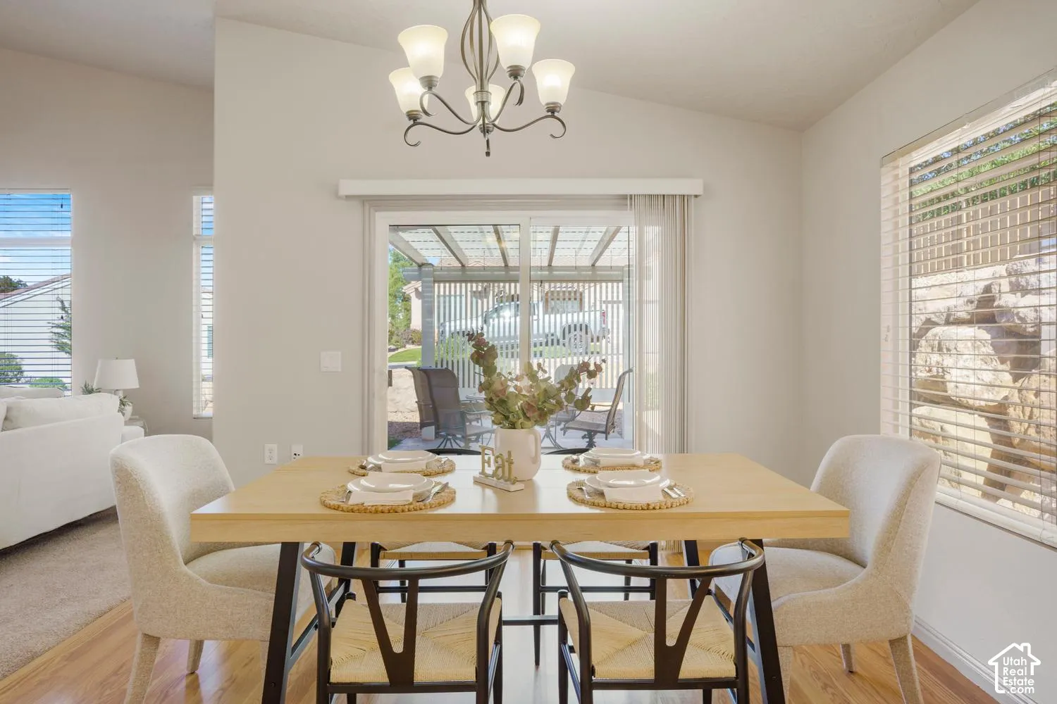 Vaulted ceiling, multi-light chandelier, wood-finish flooring, and sliding glass doors with exterior pergola