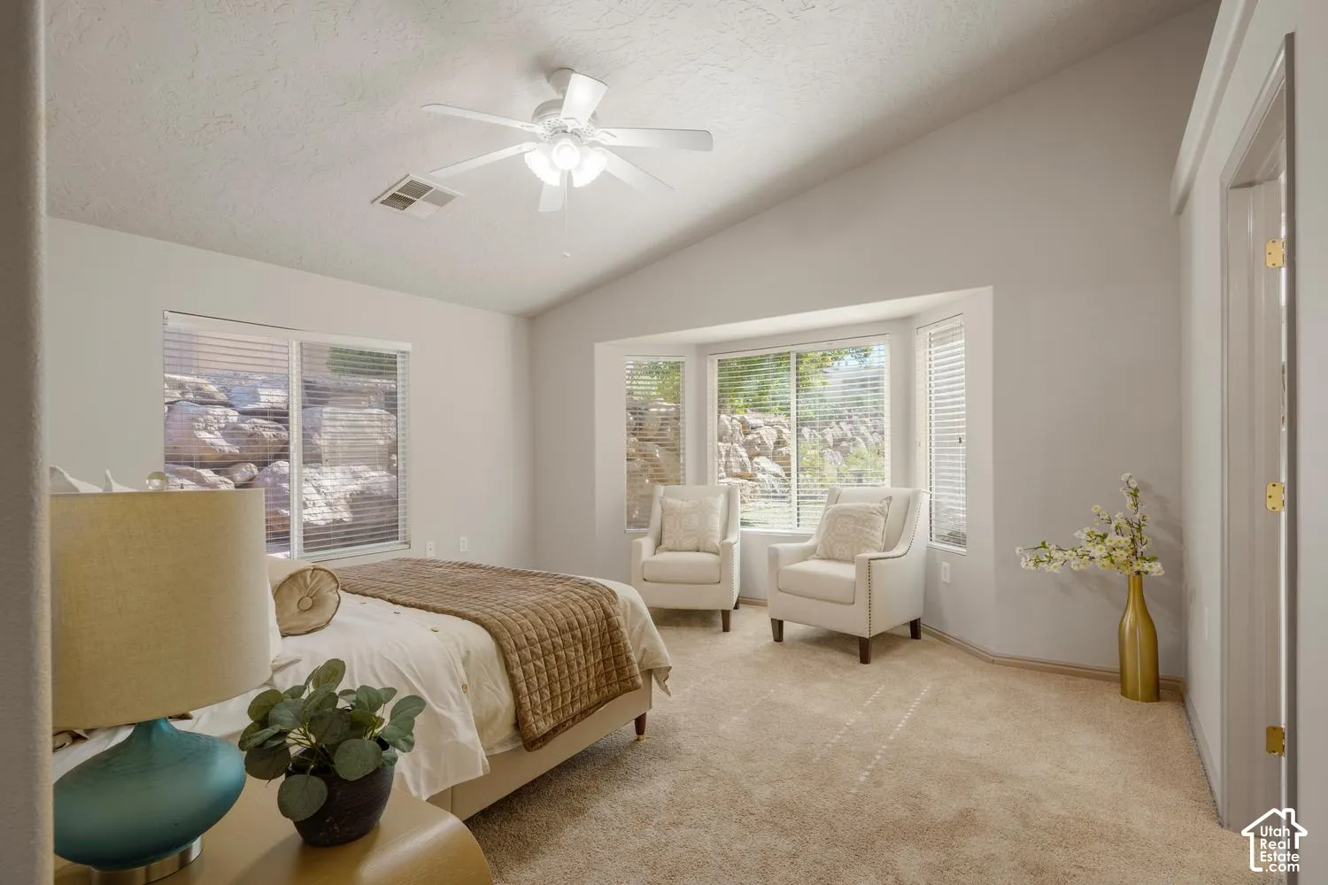 Vaulted ceilings, carpeted flooring, multi-pane bay window, and a ceiling-mounted light fixture with fan