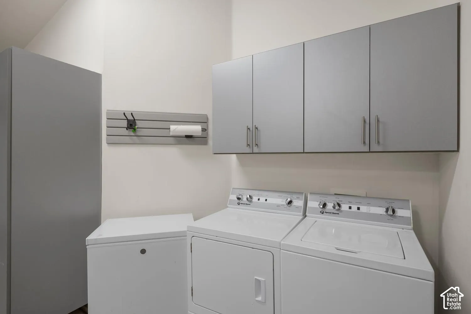 Laundry area featuring matte grey upper cabinetry, integrated slat-wall organizational system, and a full-height utility cabinet