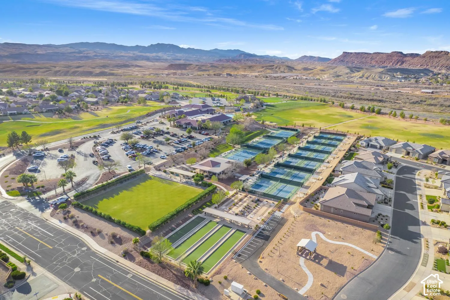 Aerial perspective featuring multi-court tennis facilities, bocce ball courts, expansive manicured lawn, and mountain scenery