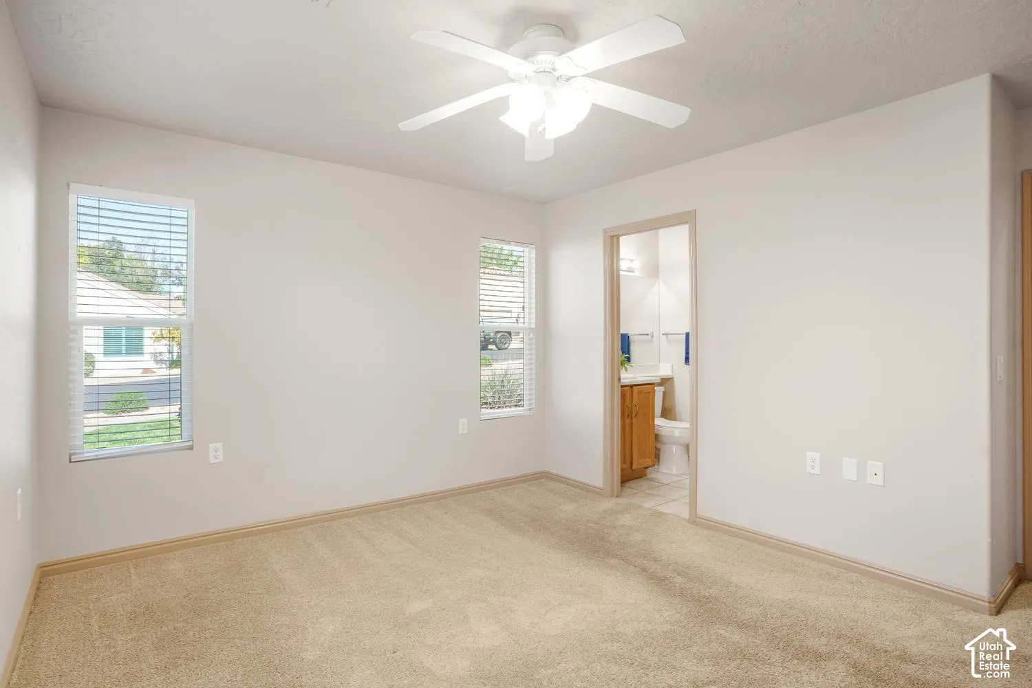 Room featuring neutral wall tones, wall-to-wall carpeting, dual windows with horizontal blinds, and a multi-blade ceiling fan with integrated lighting