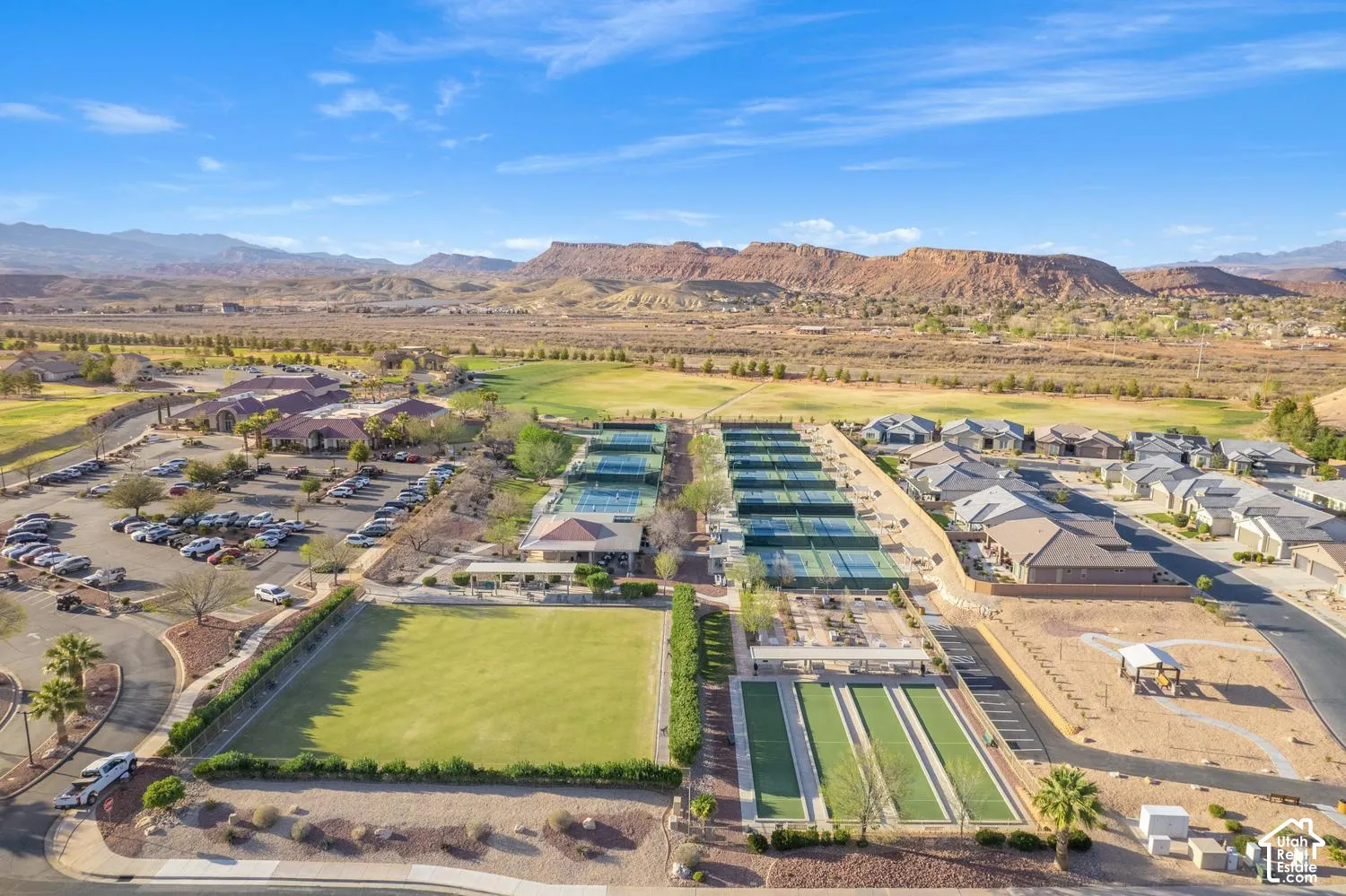 Aerial view of recreational grounds featuring multiple tennis courts, a manicured lawn area, bocce ball courts, and a covered pavilion, set against a mountainous desert landscape