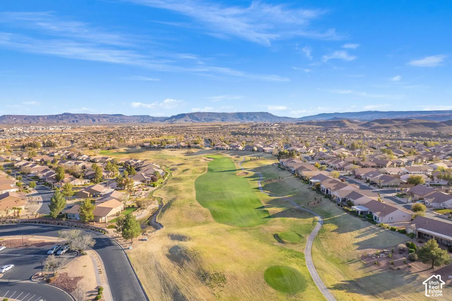 Aerial perspective of a residential community featuring a golf course fairway, paved cart paths, arid desert landscaping, and prominent mountain backdrops