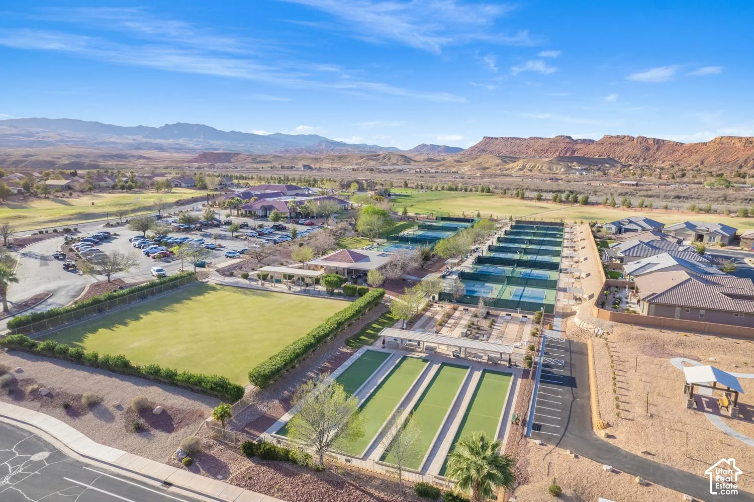 Aerial perspective of community recreation grounds featuring tennis courts, bocce ball lanes, expansive lawn space, and mountain backdrop