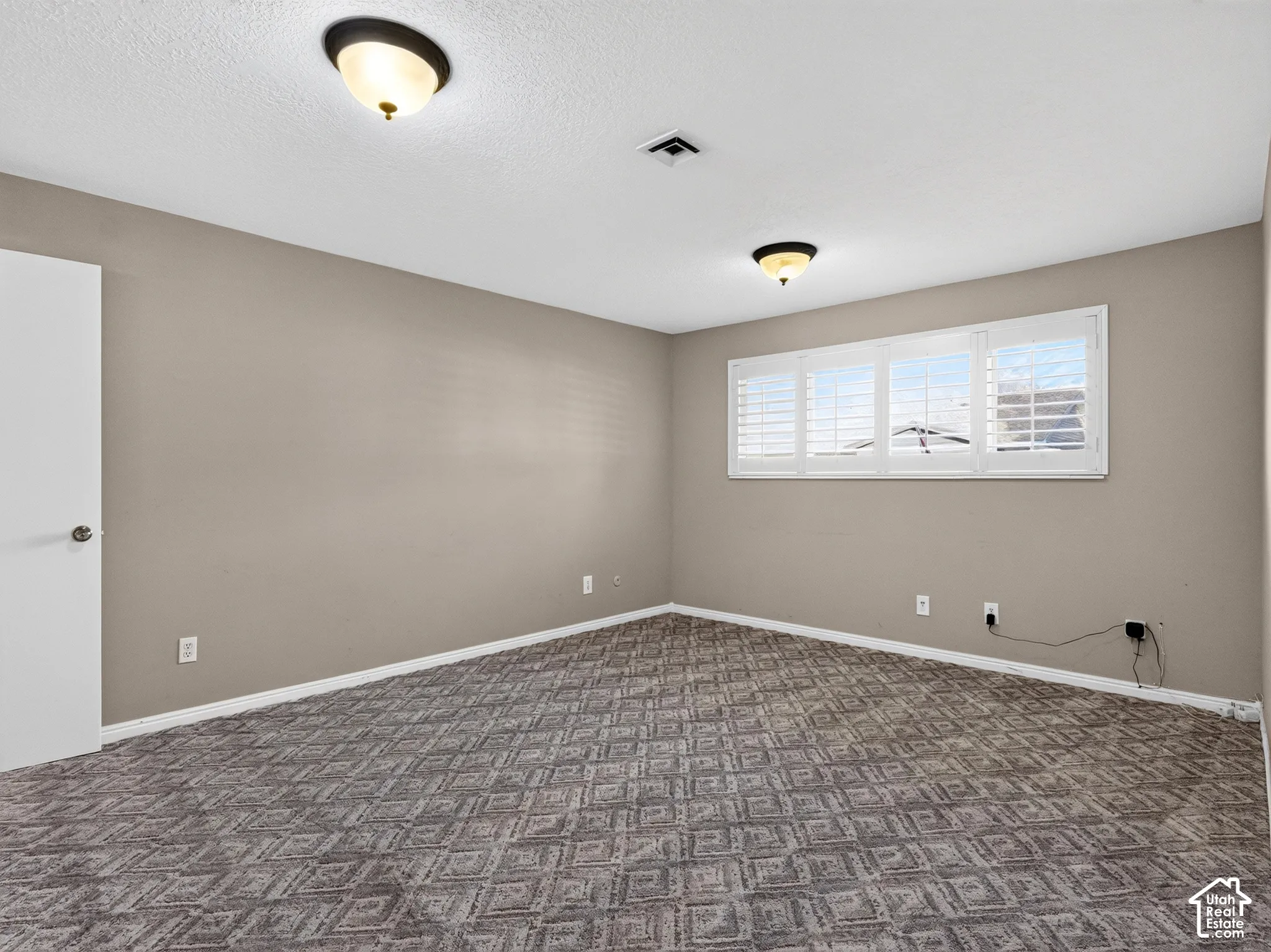 Neutral wall tones featuring textured carpeting, dual flush-mount light fixtures, and white plantation shutters