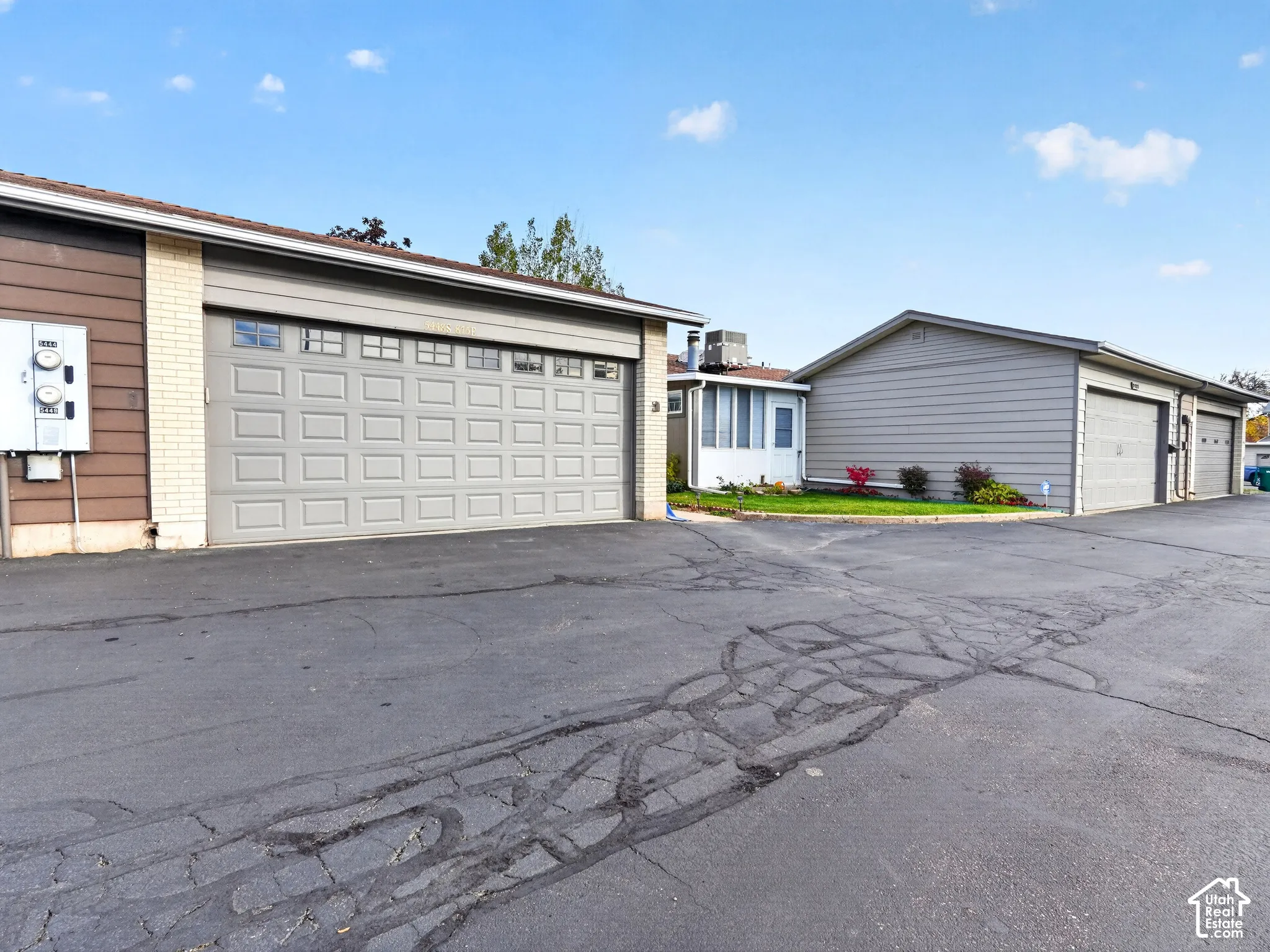 Exterior view featuring multiple garages with paneled doors, light-colored brick and horizontal siding, and asphalt paving