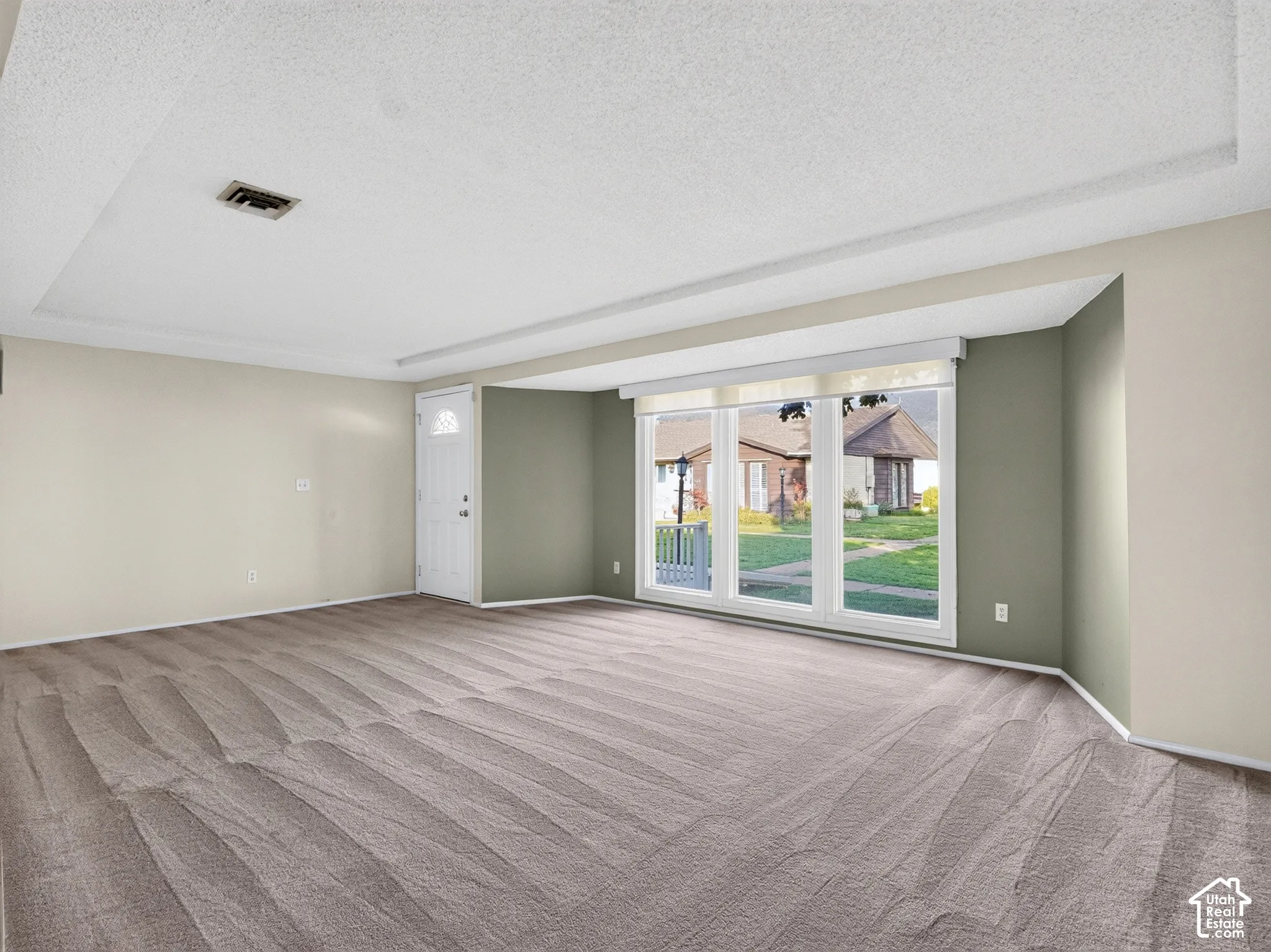 Room featuring wall-to-wall carpeting, a multi-pane window configuration with installed roller shades, an exterior door with a decorative glass insert, and an accent wall