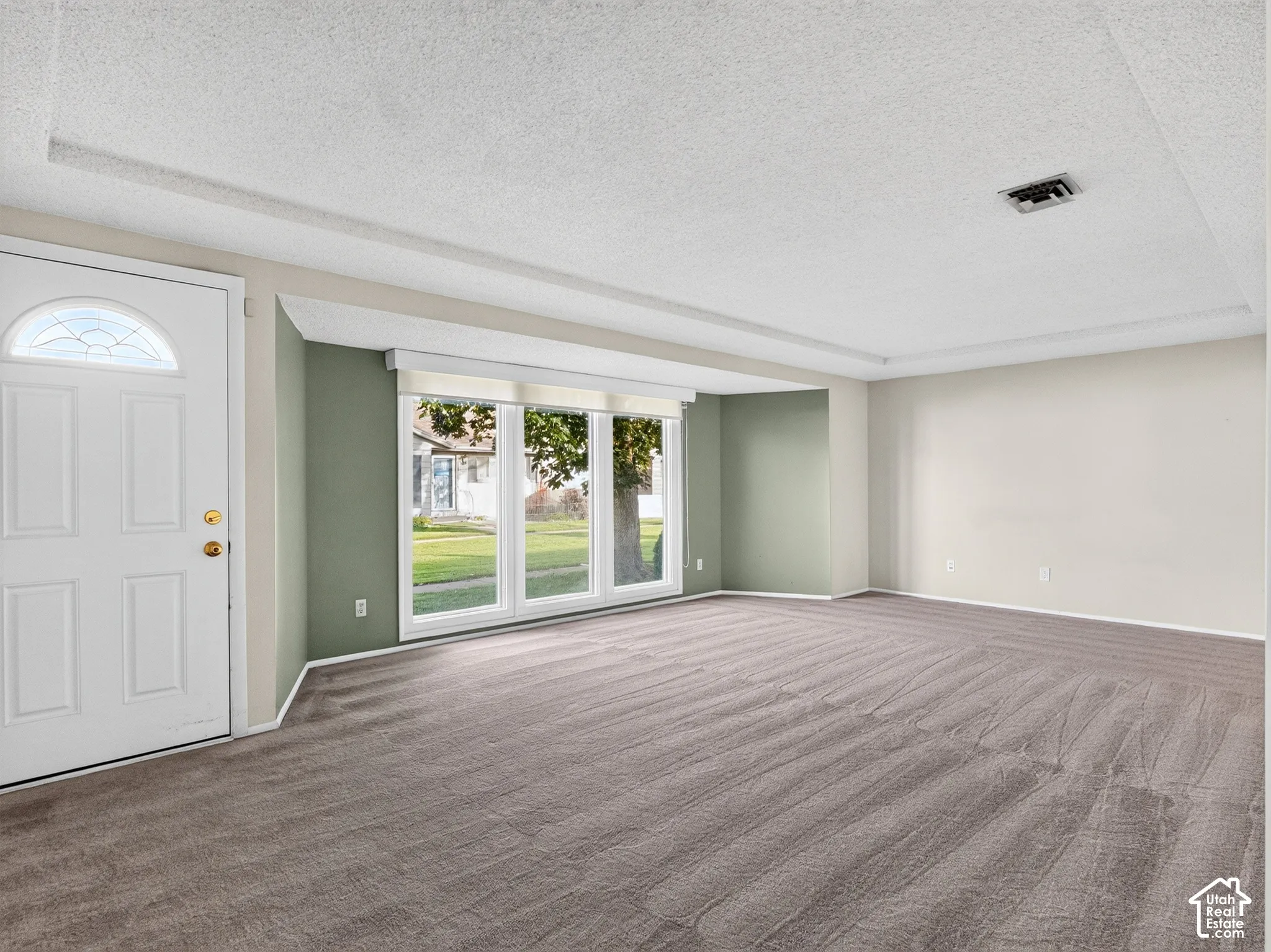 Interior space featuring neutral wall tones, textured ceiling, wall-to-wall carpeting, and a triple-pane window arrangement