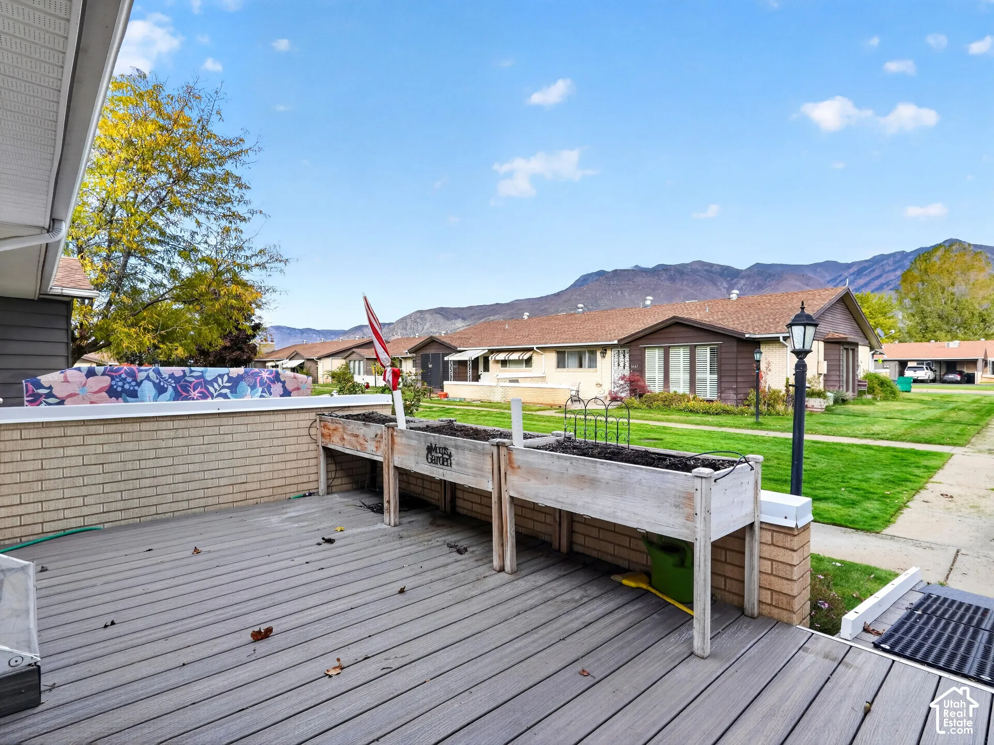 Ground-level composite deck featuring a brick perimeter wall, integrated raised garden planters, a lamp post, and mountain backdrop