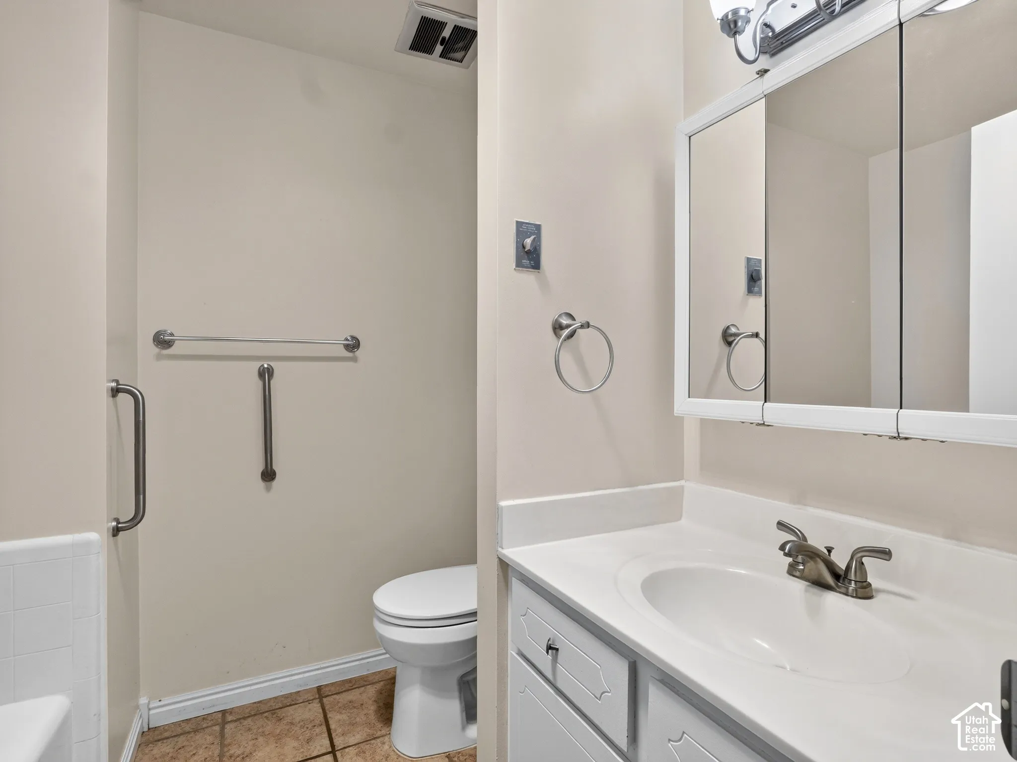 Bathroom featuring a white vanity with an integrated countertop, tri-fold medicine cabinet, neutral-toned floor tile, and brushed metal hardware