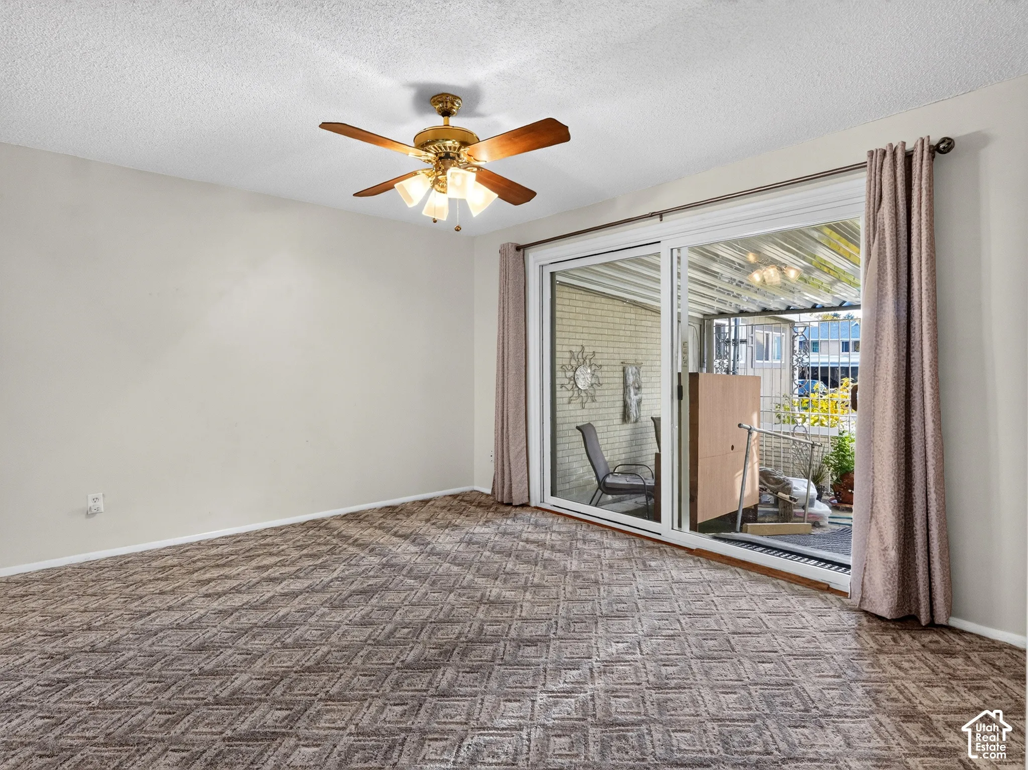 Interior space featuring textured carpeting, neutral wall color, overhead ceiling fan with light fixture, and sliding glass door