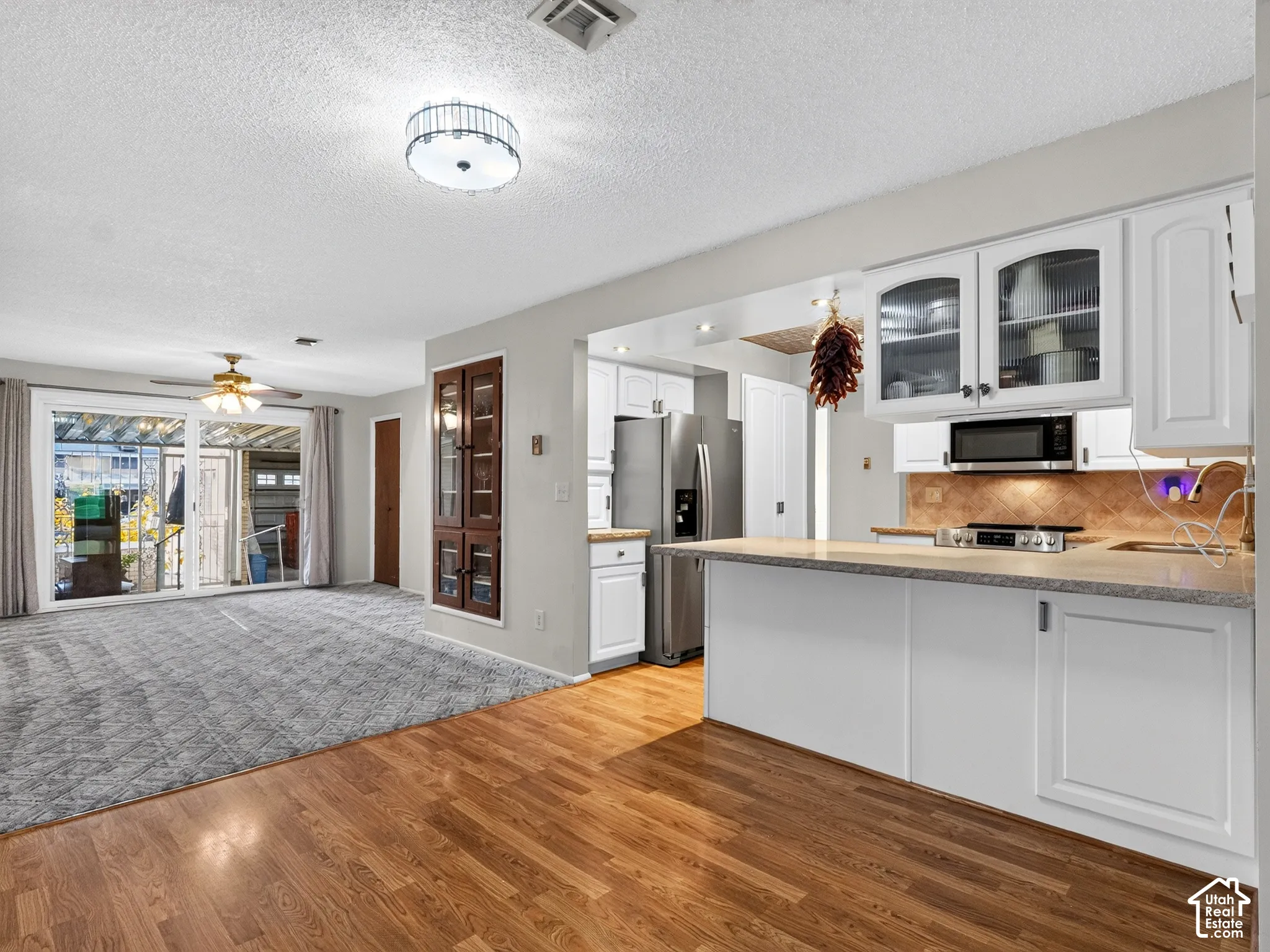 Kitchen featuring white cabinetry, stone-surface countertops, built-in microwave, and stainless steel refrigerator, complemented by wood-finish flooring