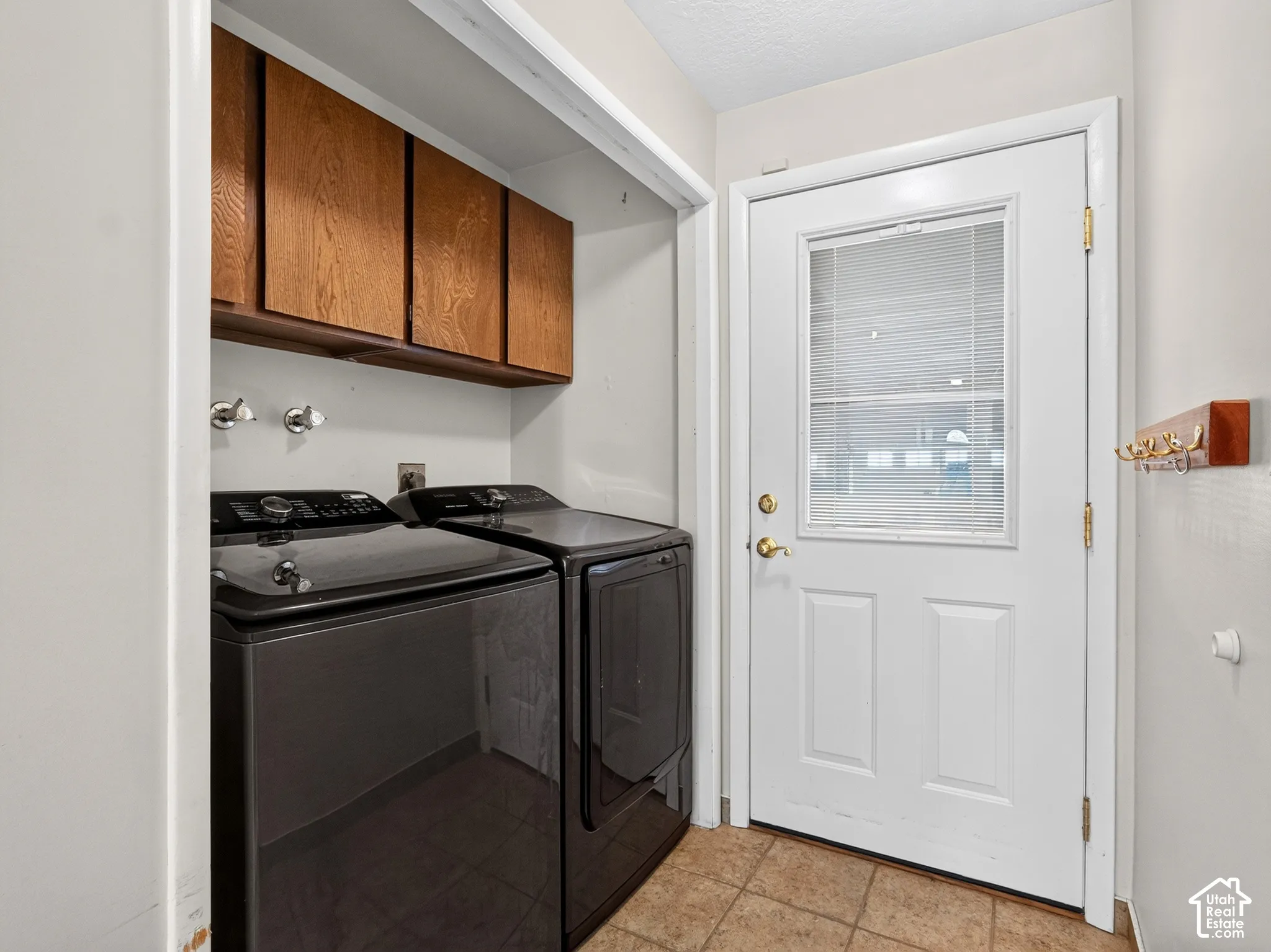 Utility area featuring ceramic tile flooring, upper wood-finish cabinetry, and an exterior door with a glass pane