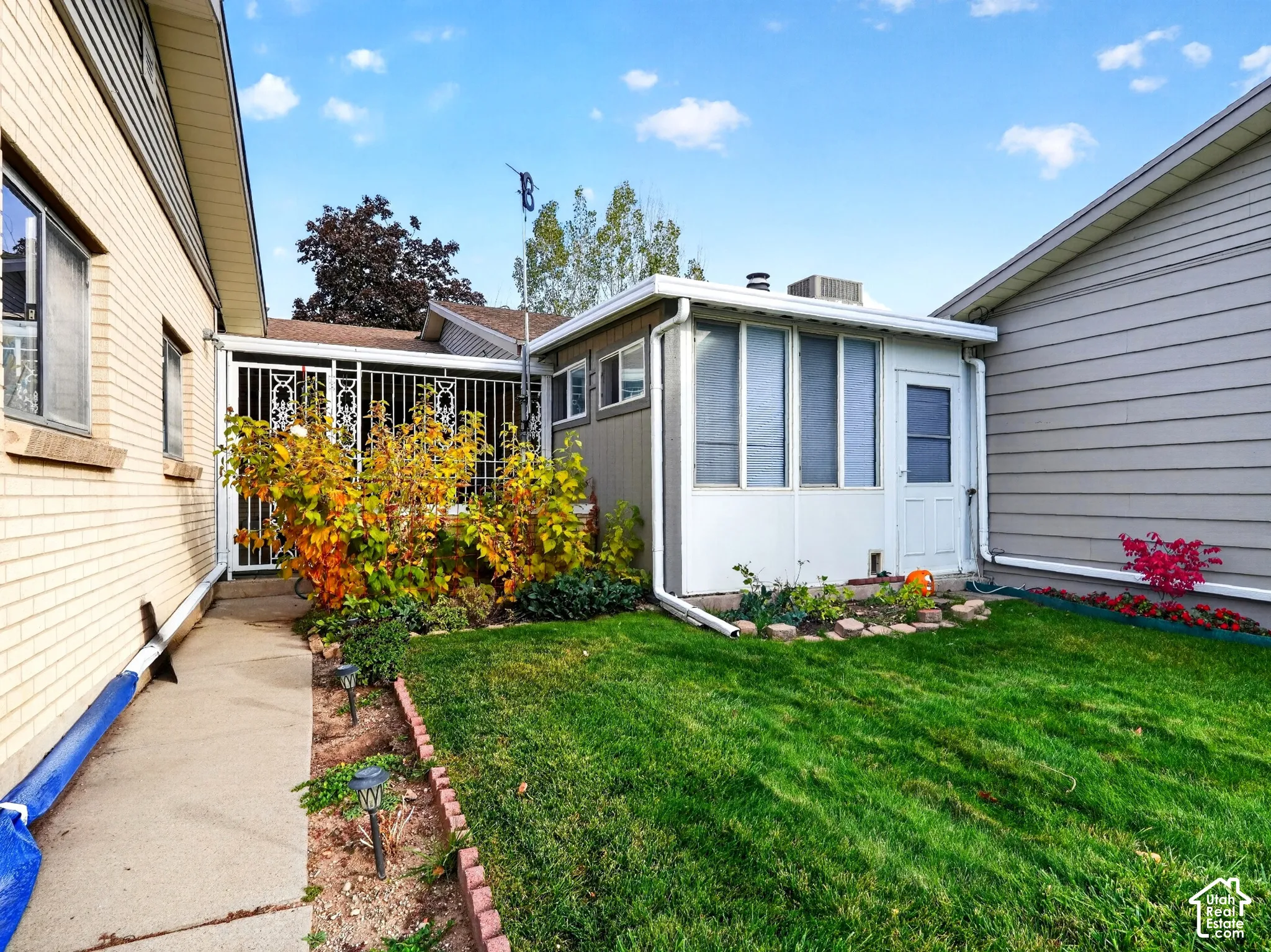 Enclosed sunroom featuring white window frames and a private entry door, concrete walkway, and decorative metal security screening