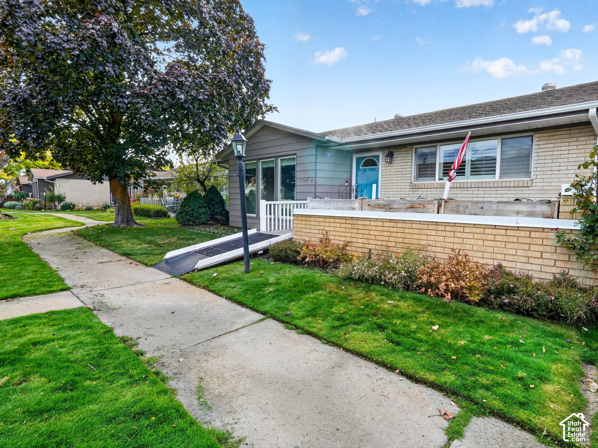 Single-story exterior featuring a brick facade, siding accents, a metal ramp, and a low-profile stone retaining wall