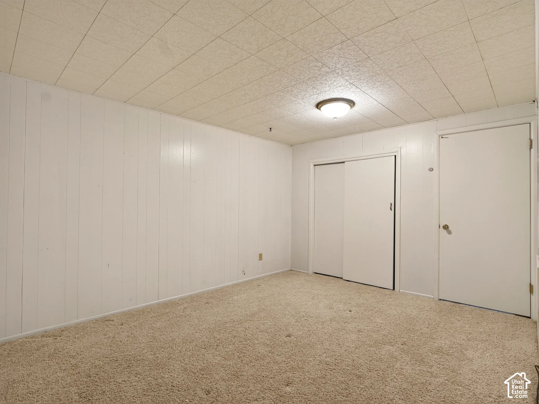 Room featuring carpeted flooring, white vertical wall paneling, a drop ceiling, and a built-in sliding door closet