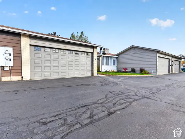 Exterior view featuring multiple garages with paneled doors, light-colored brick and horizontal siding, and asphalt paving