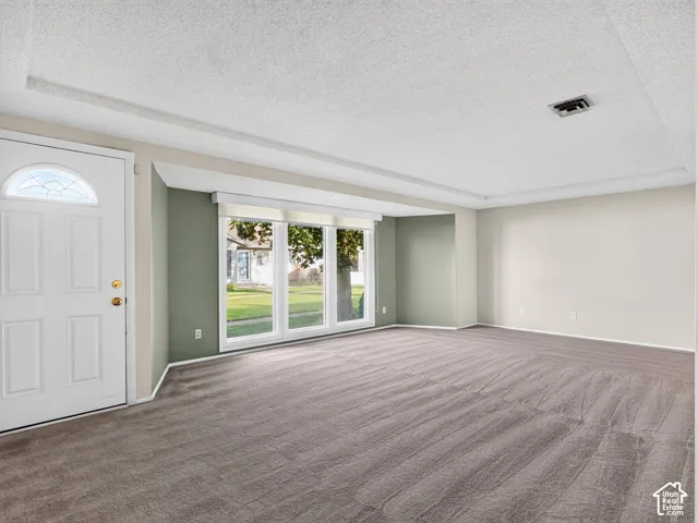 Interior space featuring neutral wall tones, textured ceiling, wall-to-wall carpeting, and a triple-pane window arrangement