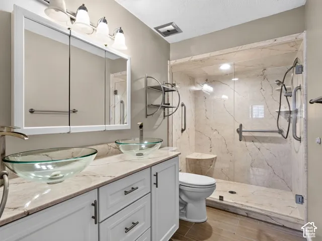 Bathroom featuring white shaker-style cabinetry, dual glass vessel sinks with stone-finish countertops, and a walk-in shower with integrated bench seating and stone-style wall surround