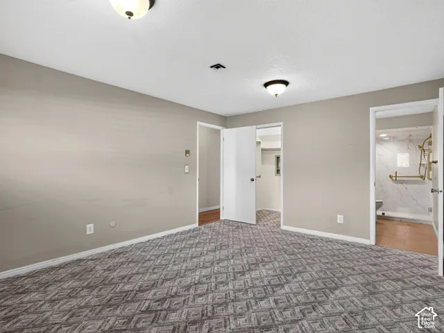 Bedroom featuring patterned carpeting, neutral wall paint, dual flush-mount ceiling light fixtures, and a walk-in closet