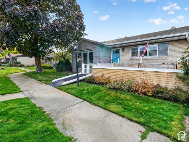 Single-story exterior featuring a brick facade, siding accents, a metal ramp, and a low-profile stone retaining wall