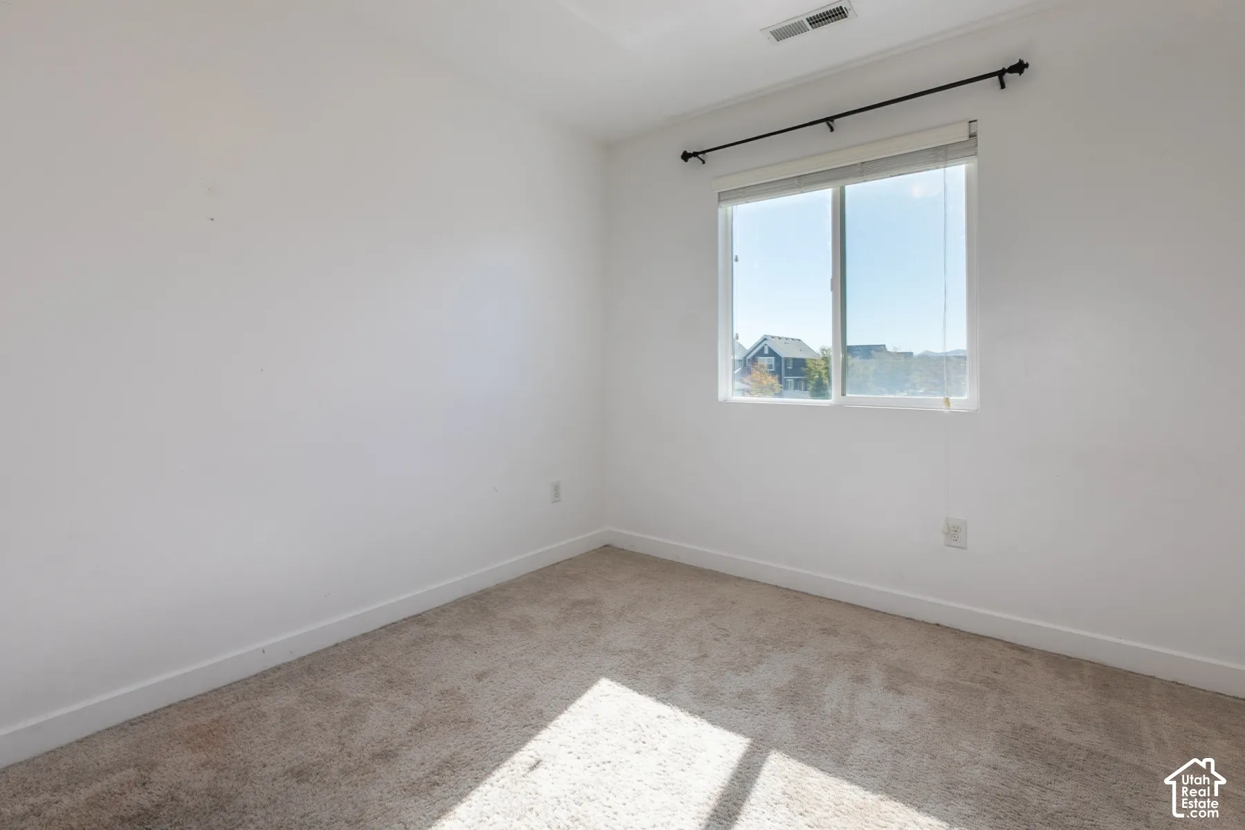 Neutral-toned carpeting, white walls, and a large sliding window with a mounted curtain rod