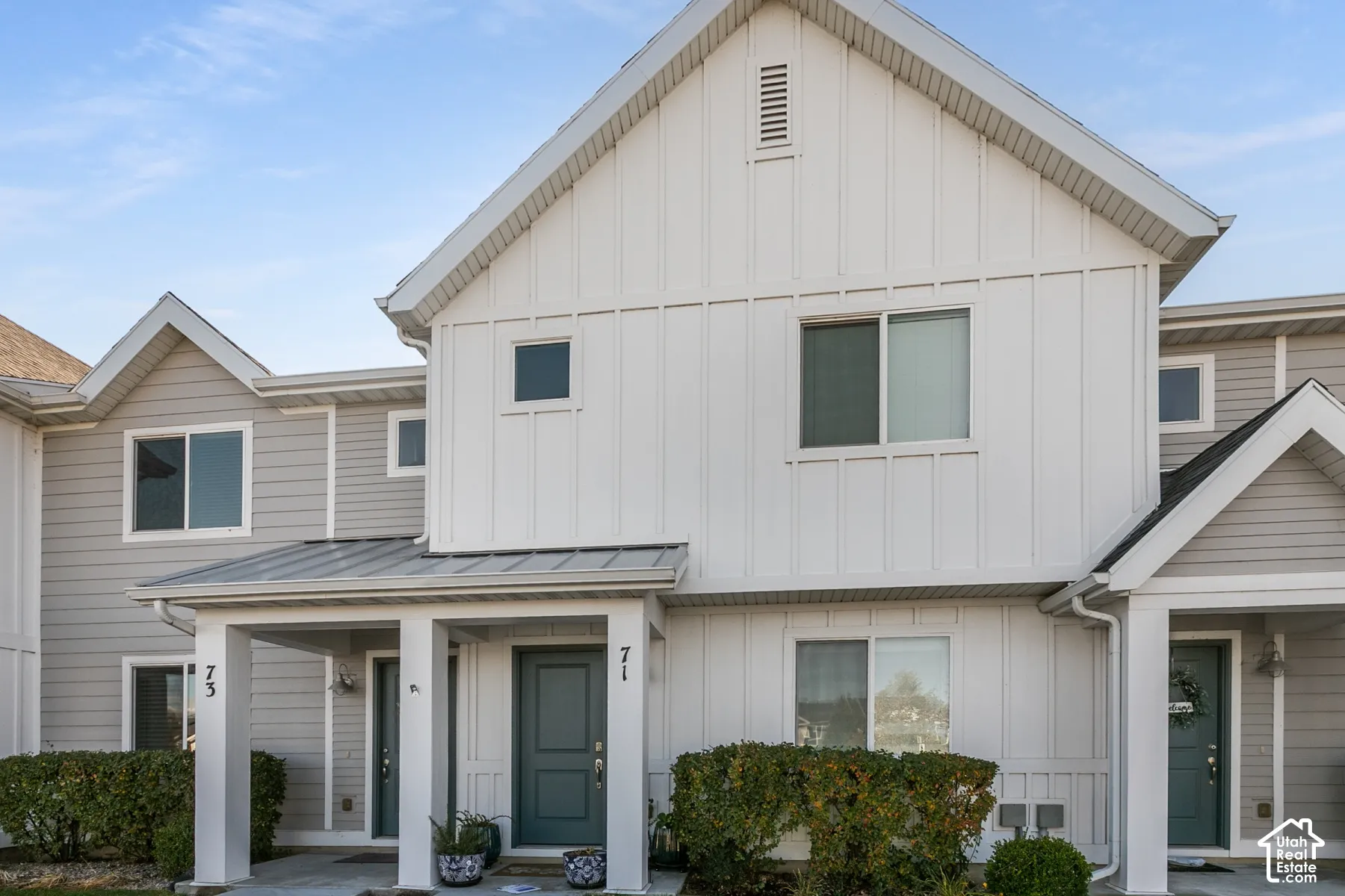Multi-unit exterior featuring vertical board-and-batten and horizontal lap siding, a metal-roofed covered entryway, and gable rooflines