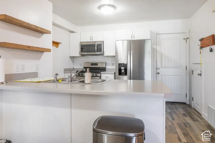 Kitchen featuring white shaker-style cabinetry, stainless steel appliances, wood-finish flooring, and natural wood floating shelving