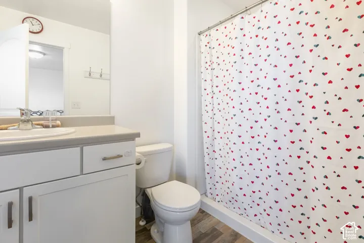 Bathroom featuring white cabinetry, integrated sink, wood-finish flooring, and a shower-tub combination with a curtain rod