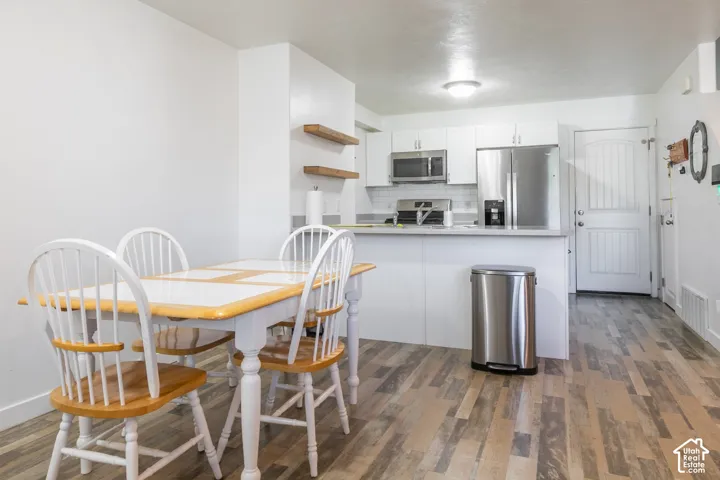 Kitchen featuring white cabinetry, stainless steel appliances, wood-finish flooring, a breakfast bar, and wall-mounted floating wood shelves