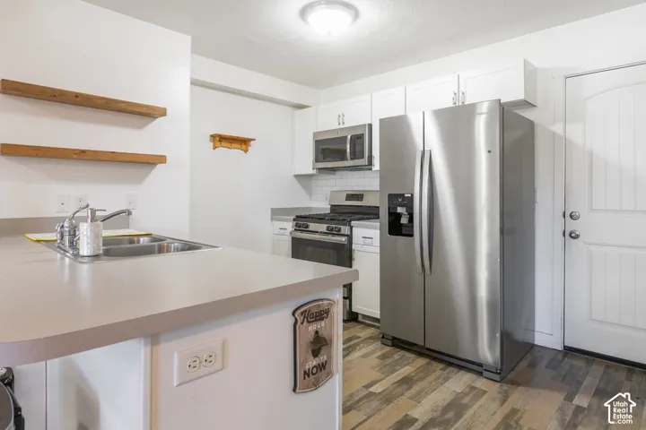 Kitchen featuring white cabinetry, stainless steel appliances, wood-finish flooring, dual-basin sink, and open wall-mounted shelving